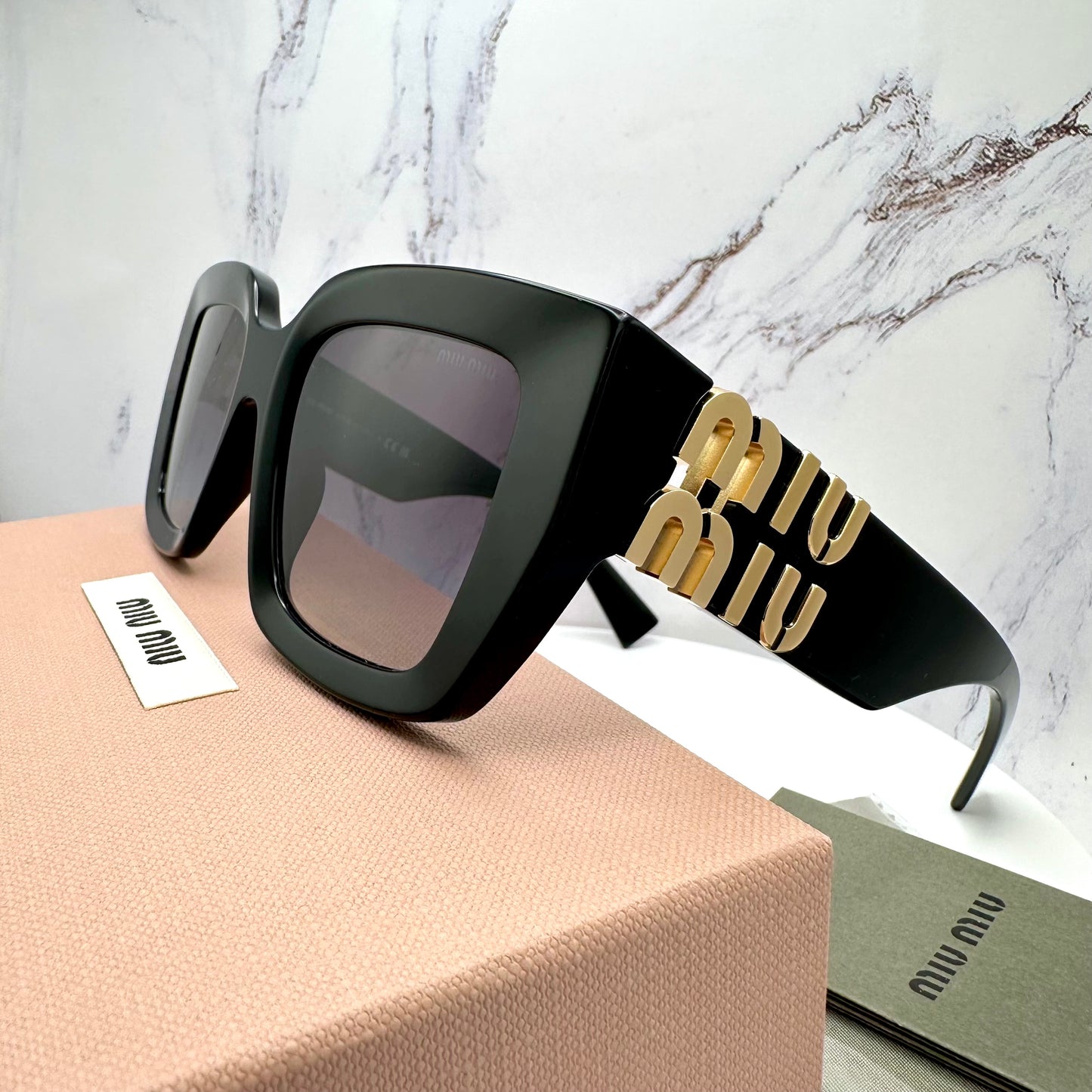 MUB05S 16K90A Miu Miu black sunglasses with gold accents on a marble background