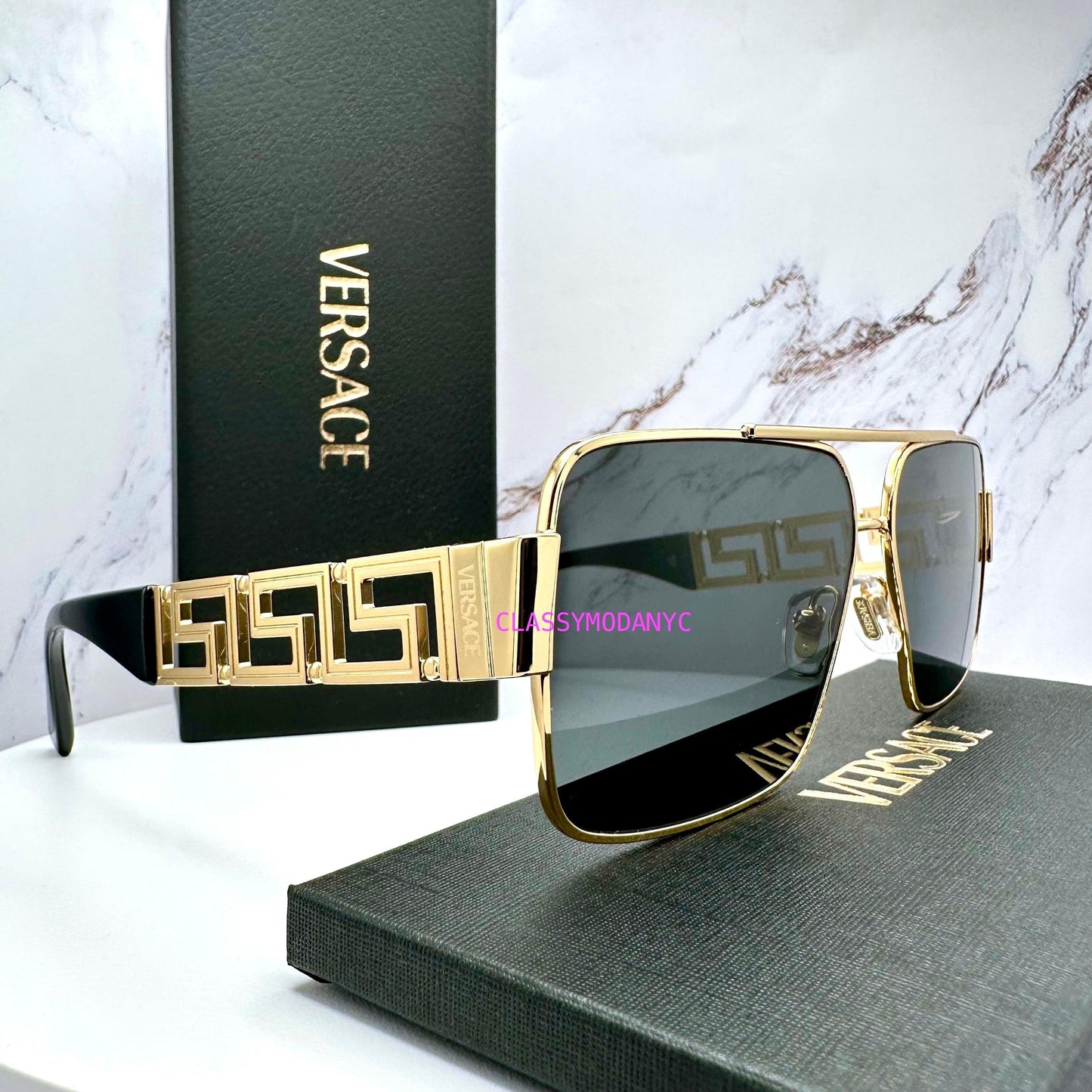 Versace sunglasses with gold frame and grey lenses on a Versace box with marble background
